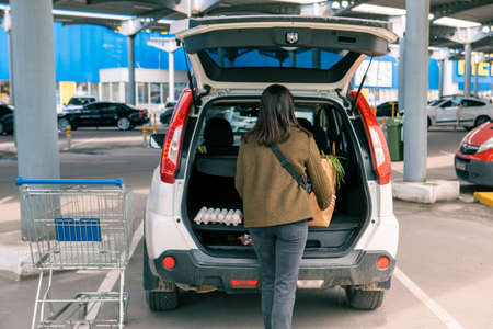 woman put bags with products in car trunk after grocery store copy space