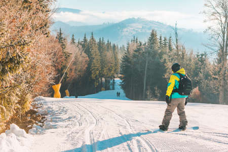 man walking by hill with snowboard mountains on backgroundの写真素材