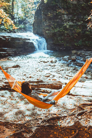 woman laying on hammock with view of autumn waterfall sunny warm day hiking conceptの写真素材