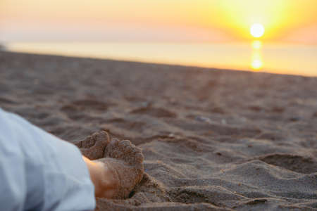woman legs in sand close up. sunset above the sea. copy spaceの写真素材