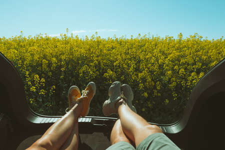 couple laying in boot car trunk looking at rapeseed field road trip