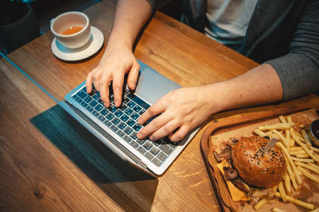 overhead view hands type on keyboard wooden table burger with mug of teaの写真素材