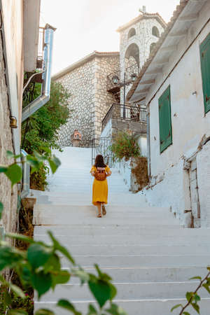 Young traveller woman in yellow dress back view walking in old greece town.の写真素材
