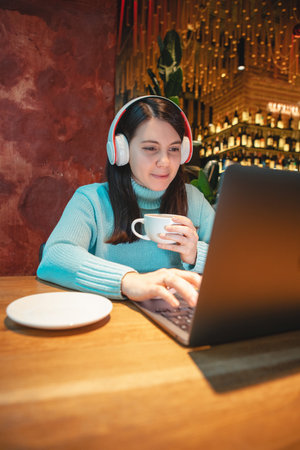 woman freelancer working on laptop in cafe drinking tea eating burgerの写真素材