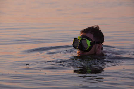 man with snorkeling mask in water on sunset