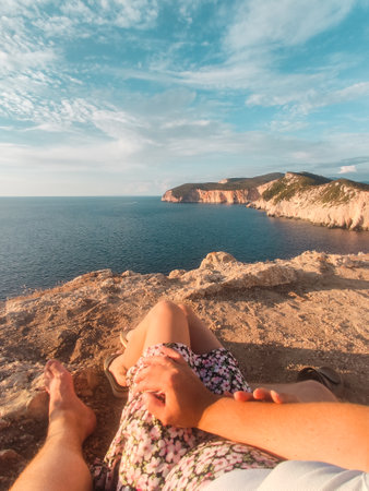 couple sitting on the cliff enjoying view of sunset above the seaの写真素材