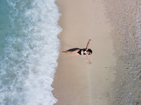 overhead view of woman in black swimsuit sunbathing at sea shoreの写真素材