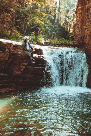 hiker woman enjoying waterfall in autumn forestの写真素材