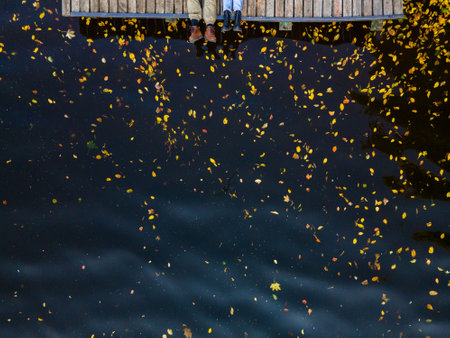 overhead view of couple legs at the wooden pier lake water with yellow leaves