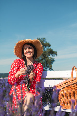 a young woman in a straw hat sits on a bench in a lavender field and weaves a wreathの写真素材