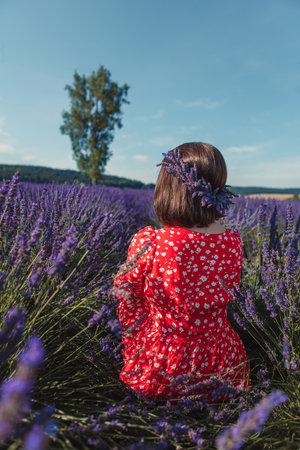 a young woman in a wreath on her head sits on a lavender fieldの写真素材