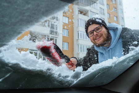 smiling bearded man cleans the car from snow inside viewの写真素材
