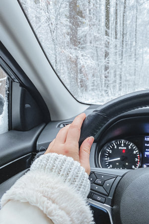 A snowy landscape outside the window with female hands on the wheel of a car