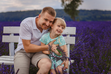 father and daughter are sitting on a bench in a lavender fieldの写真素材