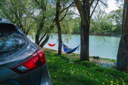 Relaxing work environment: man in hammock with laptop by riverの写真素材