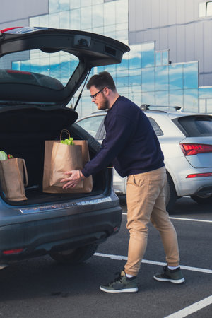 happy man put groceries bag in car trunkの写真素材