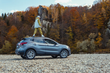 happy woman at car roof enjoying the view of autumn river in carpathian mountains