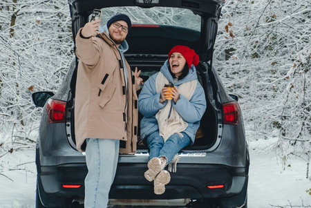 In a snowy forest, a couple stops to eat and takes a selfie next to their carの写真素材