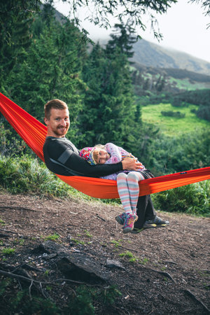 happy father with daughter on hammock mountains on background