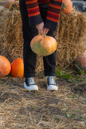 Person holding a large orange pumpkin by the stemの写真素材