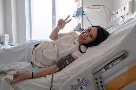 Smiling Patient in Hospital Bed Making Peace Signの写真素材