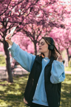 happy woman listening music in headset outdoors taking selfie with sakura on backgroundの写真素材