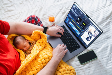 Man multitasking with laptop and baby on bedの写真素材