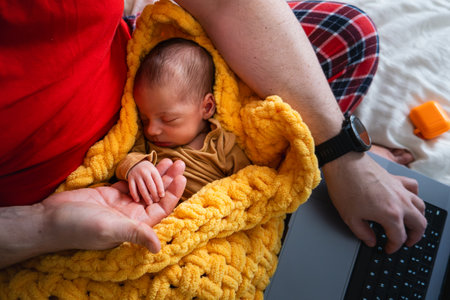 Man multitasking with laptop and baby on bedの写真素材