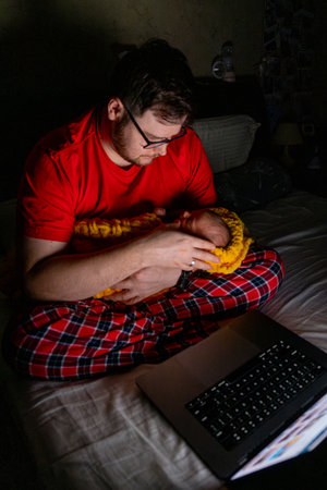 Father Holding Baby While Using Laptop in Dim Lightの写真素材