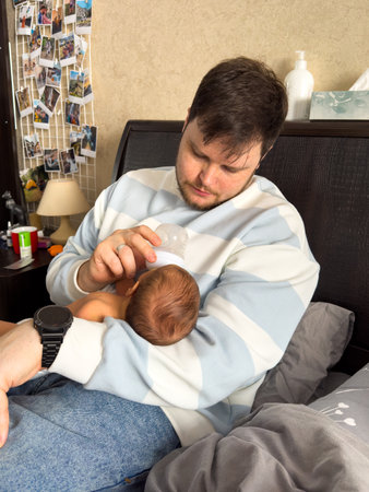 Tender Moment: Man Feeding Baby on Bedの写真素材