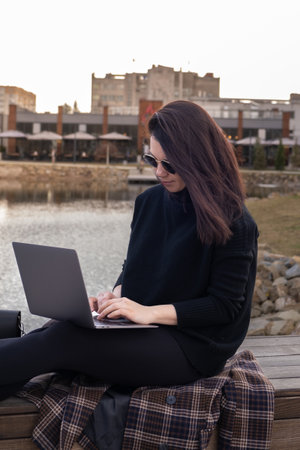 Woman Using Laptop by Pond in Urban Settingの写真素材
