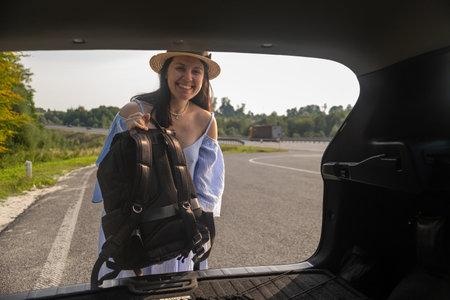 Smiling Woman with Backpack by Car on Scenic Roadの写真素材