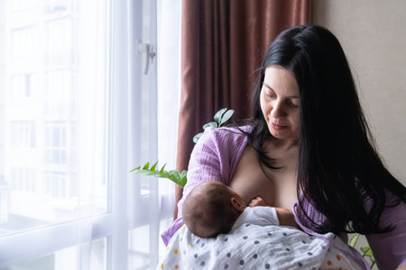 Mother Breastfeeding Baby by Windowの写真素材