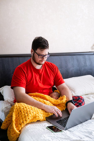 Man multitasking with laptop and baby on bedの写真素材