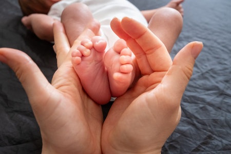 Tender Moment: Adult Hands Holding Newborn Baby Feetの写真素材