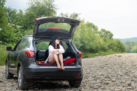 Woman Relaxing in SUV Trunk on Rocky Pathの写真素材