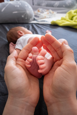 Tender Moment: Adult Hands Holding Newborn Baby Feetの写真素材