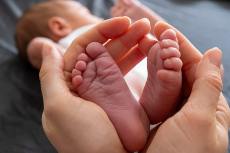 Tender Moment: Adult Hands Holding Newborn Baby Feetの写真素材