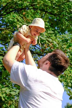 Father Lifting Baby Under Tree