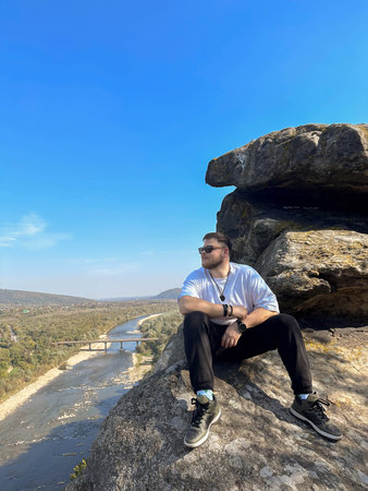 Man Sitting on Cliff Overlooking River and Valley