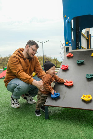 Father Assisting Toddler on Playground Climbing Wall