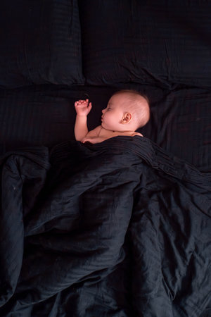 Peaceful baby sleeping on dark bedding