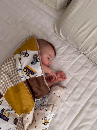 Peaceful sleeping baby under patchwork quilt on white bed