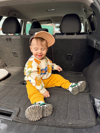 Toddler sitting in open car trunk during family road trip