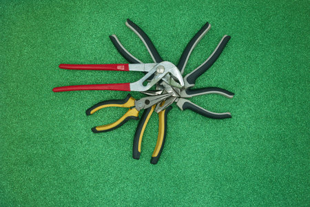 Pliers and pruning shears on green background. top view.