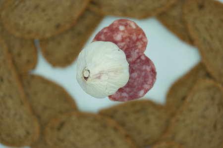 sliced salami and garlic on a white plate with breadの写真素材