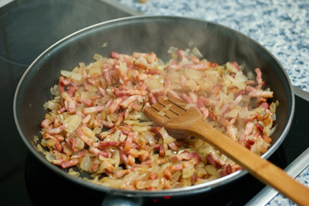 Fried onions in a frying pan with a wooden spatula.の写真素材