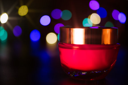 a jar of cosmetic cream on a black background illuminated with colored lightsの写真素材