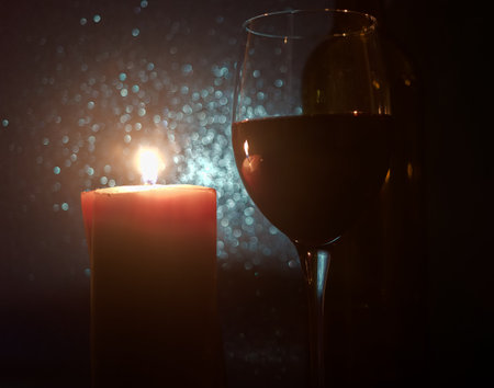 a burning candle on the side of a glass of wine and a bottleの写真素材