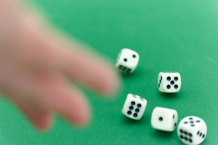 A hand reaches for several white dice laid out on a green surface amid a friendly game atmosphere. The dice display unique number patterns, enhancing the playful vibe.の写真素材